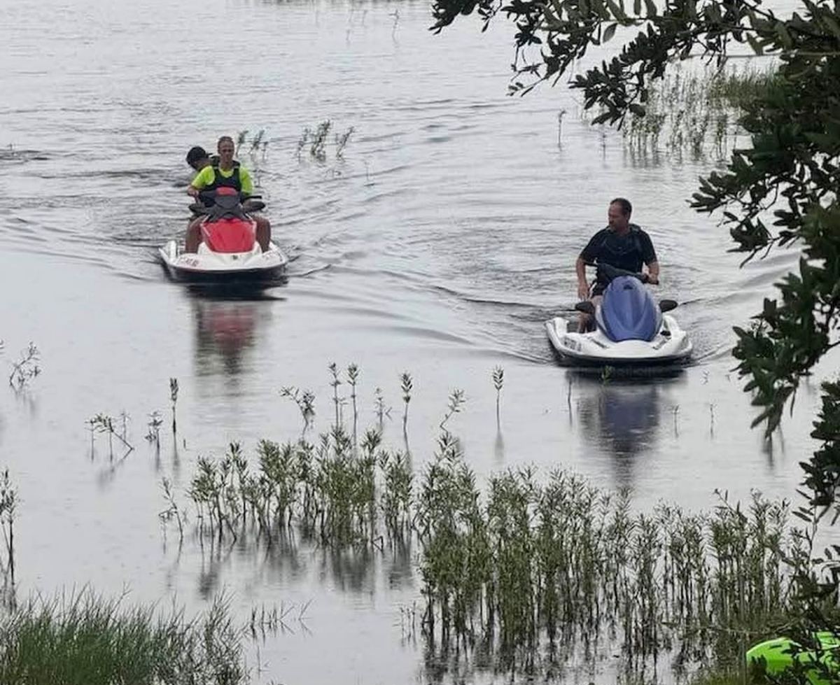 Two riders on PWCs idling through shallow water on the lake